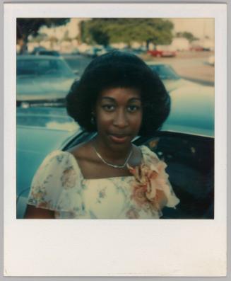 [Woman with coiffed hair wearing floral dress and pink corsage]
