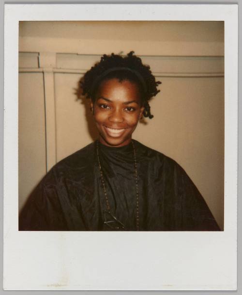 [Woman smiling wearing black hairdressing apron with glasses hanging around her neck]
