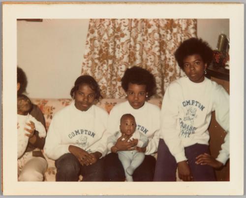 10-15-71 [Three girls sitting on couch wearing matching white Compton crewnecks, girl in middle holding baby]