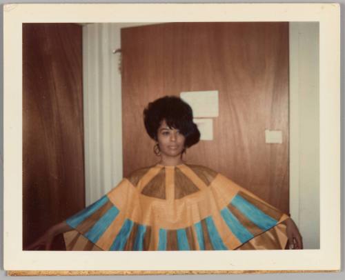 [Woman posing in front of wood door, wearing blue and tan cape dress]
