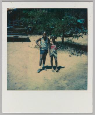 [Two girls standing on beach with truck in background]

