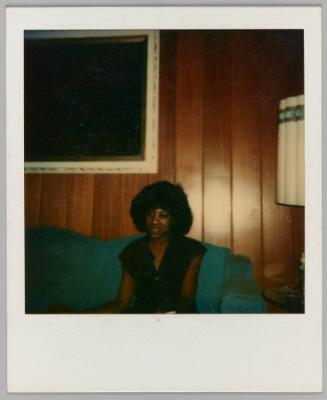 [Woman sitting on green couch in wood panelled room]
