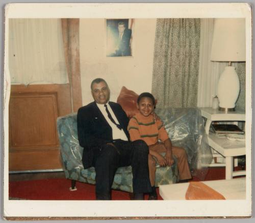 12-29-68 [Man in suit with arm around boy sitting on plastic wrapped couch]