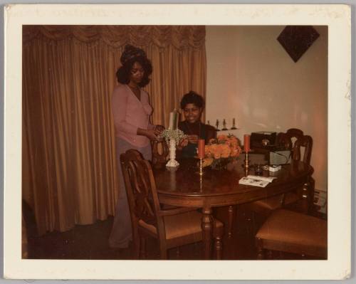 [Two women in dining room decorating a candle stick]
