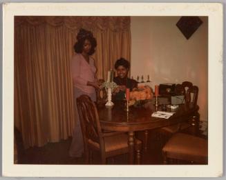 [Two women in dining room decorating a candle stick]
