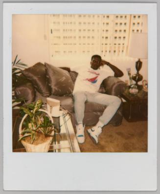 [Man wearing Nike shoes sitting in living room with plants]
