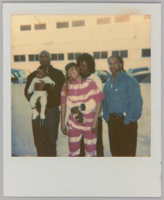 [Three men, man in centre embracing woman, man on left holding a baby]
