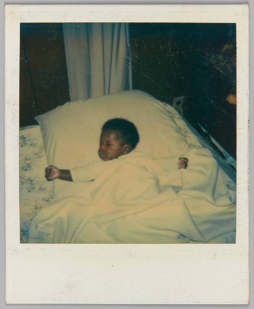 [Baby covered in blanket with arms open laying in bed]
