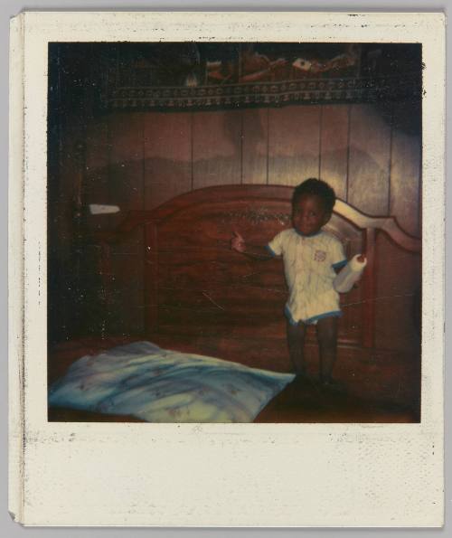 [Toddler standing on bed holding a baby bottle]
