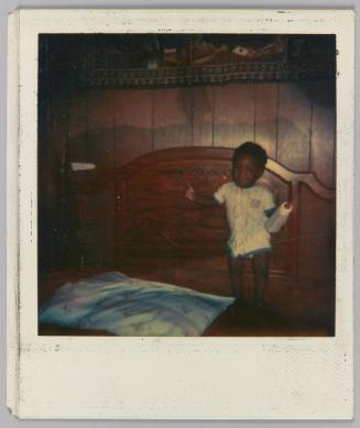 [Toddler standing on bed holding a baby bottle]
