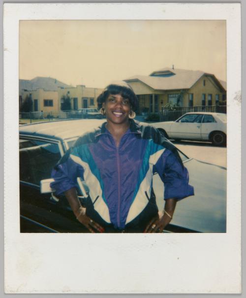 [Woman in windbreaker posing with hands on hips in front of car]
