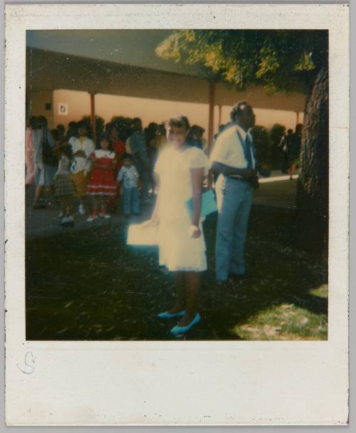 [Girl in white dress posing in front of line-up of families]
