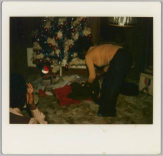 [Woman in yellow sweater unwrapping presents beneath Christmas tree]
