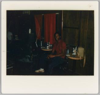 [Man sitting in chair between two side tables with beer bottles]
