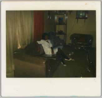 [Woman in white dress and pumps seated cross-legged on couch]
