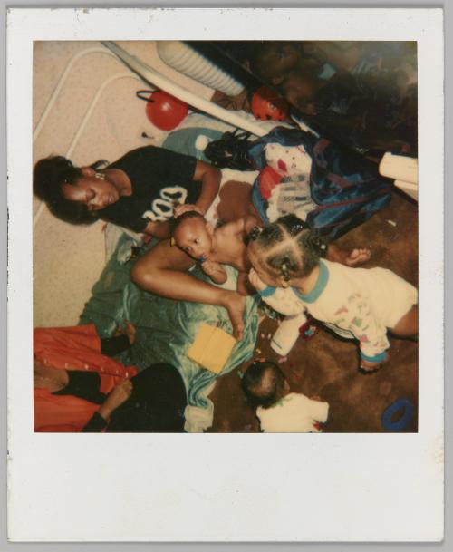 [Woman seated on bed braiding toddlers hair]
