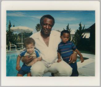 [Man seated at poolside with young boys in each arm]
