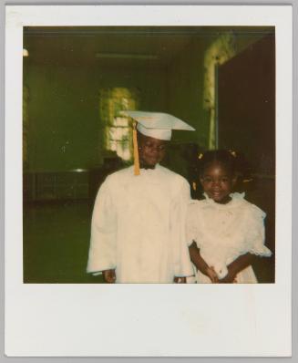 [Little boy in graduation robes posing with little girl in white dress]
