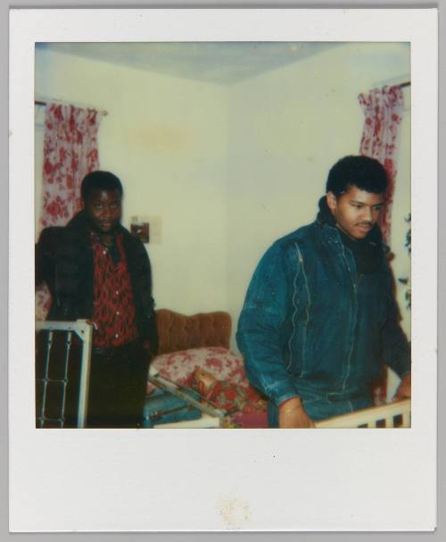[Two men in bedroom with matching red and white curtain and bedding]
