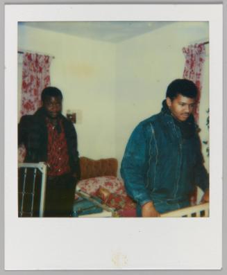 [Two men in bedroom with matching red and white curtain and bedding]
