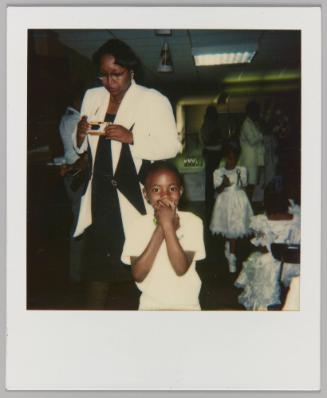 [Woman holding disposable camera and boy clasping hands over his mouth]
