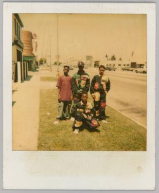 [4 adolescent boys, 3 in matching uniforms on grass strip beside road]
