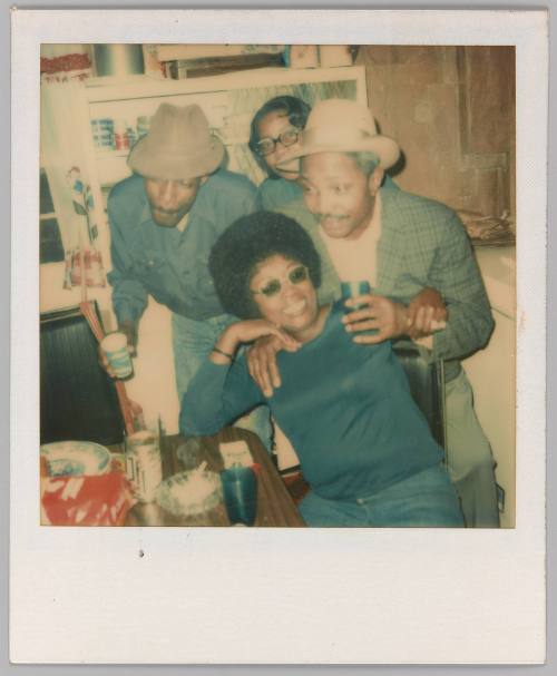 [Two men with fedoras, two women with glasses partying in kitchen]
