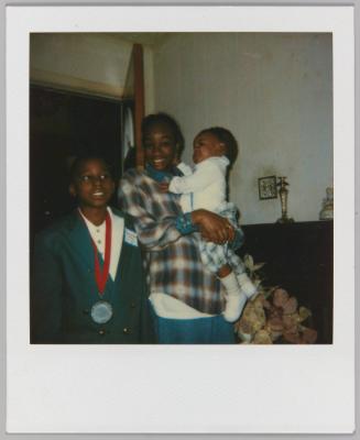 [Two boys and a baby, boy on left wearing metal around his neck]
