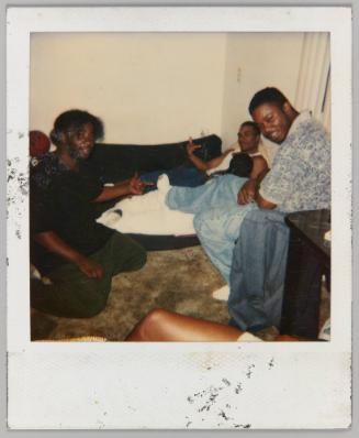 [Three young men seated in living room, man on couch flipping off the camera]
