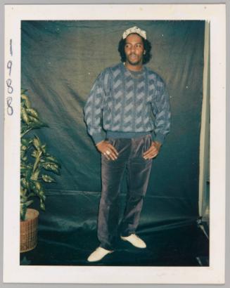 1988 [Man posing in front of black backdrop with plant]
