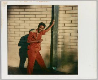 [Man leaning against drain pipe in orange outfit]
