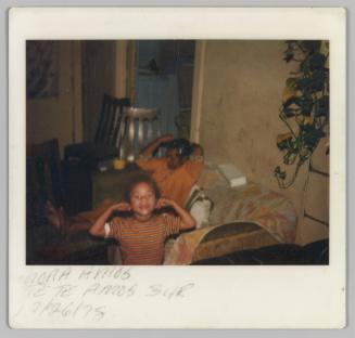 Mona Amos, Te Te Amos 3yr [Woman and child in living room; woman seated on couch; child holding ears]
