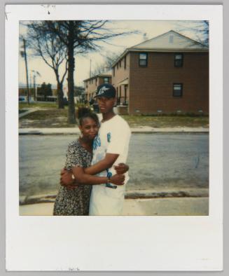 [Teen girl and teen boy embracing on the street outside of brick house]
