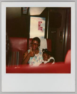 [Woman and child seated on a train; child sleeping in woman's lap]
