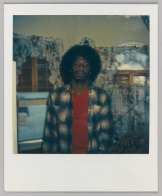 [Man posing indoors in front of floral curtains in red shirt and unbuttoned flannel shirt]
