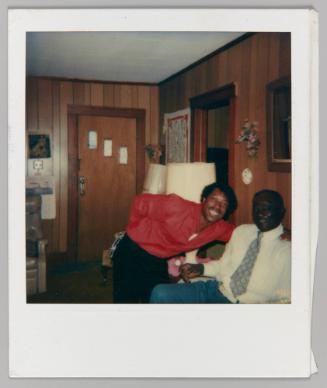 [Two men pose and smile in wood panelled living room]
