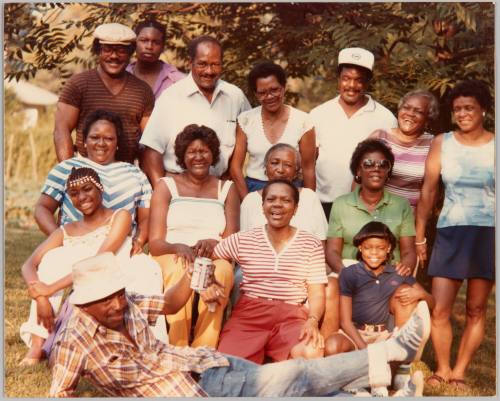July 4, 1982 [D]orton family Atlanta, Ga. [Family members posed together outside, man in front reclining and holding up a beer]
