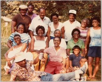 July 4, 1982 [D]orton family Atlanta, Ga. [Family members posed together outside, man in front reclining and holding up a beer]