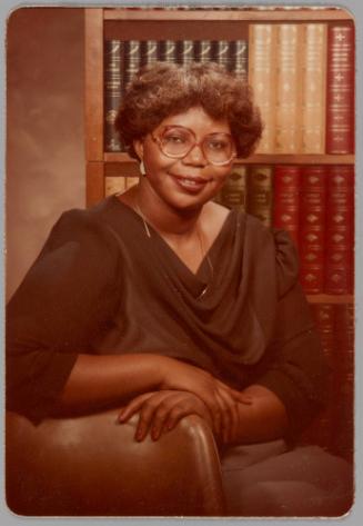 To Mom [Portrait of woman in red-rimmed glasses and a black top, she is sitting down in front of bookcase]