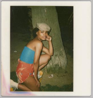 [Woman kneeling by tree trunk at night, she is wearing a blue top and cap]