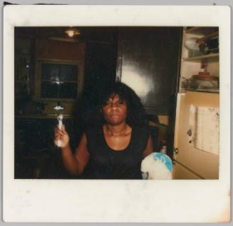 [Woman in kitchen holding a spoon in one hand and a plastic bag in the other]