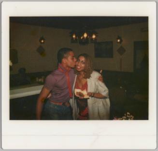 [Man kissing woman on the cheek, she is holding food in her hand]