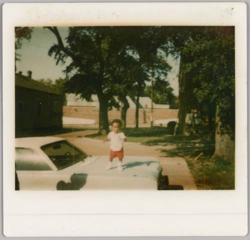 [Toddler in red shorts standing on hood of car]