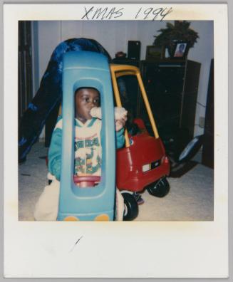 Xmas 1994 [Toddler in "Ninja Turtles" shirt sitting in toy car and drinking from a bottle]