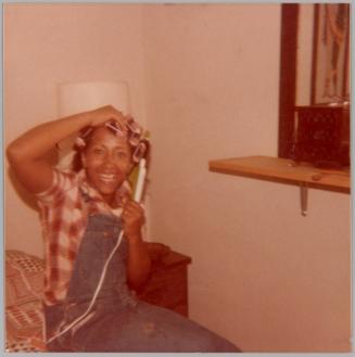 [Woman with pink curlers in hair smiling and sitting on bed]
