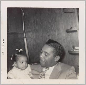 [Man holding baby and smiling as the baby holds his tie with whole fist]
