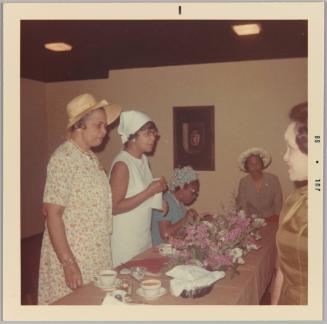 [Group of older women around a table with a pink floral centre piece]
