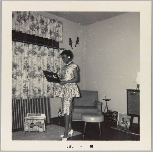 [Woman in metallic silver patterned outfit and white heels standing in living room]
