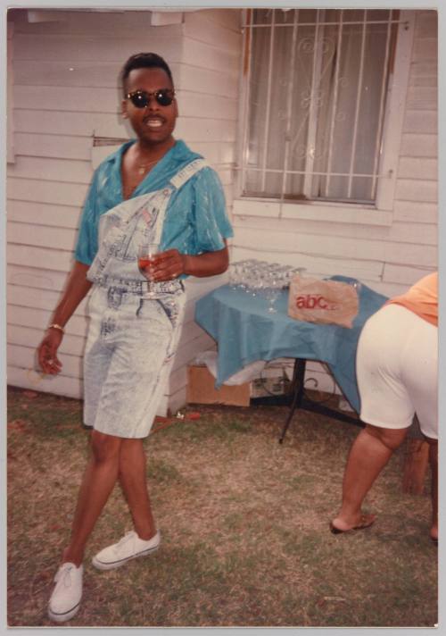 [Man posing wearing short-overalls, holding a wine glass]
