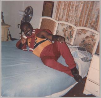 [Man outstretched in sweatsuit on bed smiling on the telephone]
